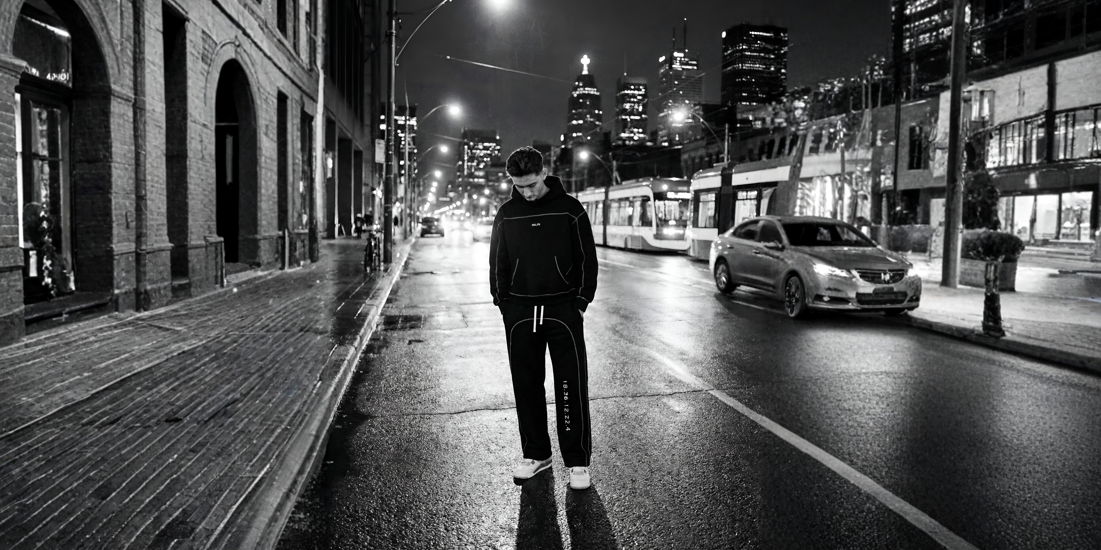Person wearing RZLVD gear, walking on a city street at night with illuminated buildings in the background